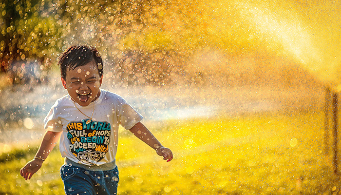 boy running in shower of water from sprinkler
