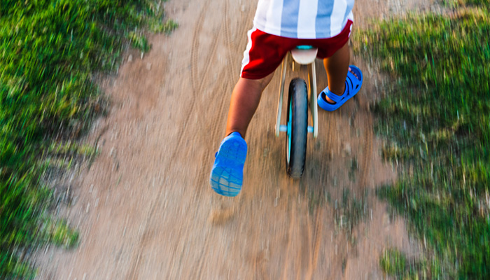  boy on a small bike using his feet on the dirt track to move forward