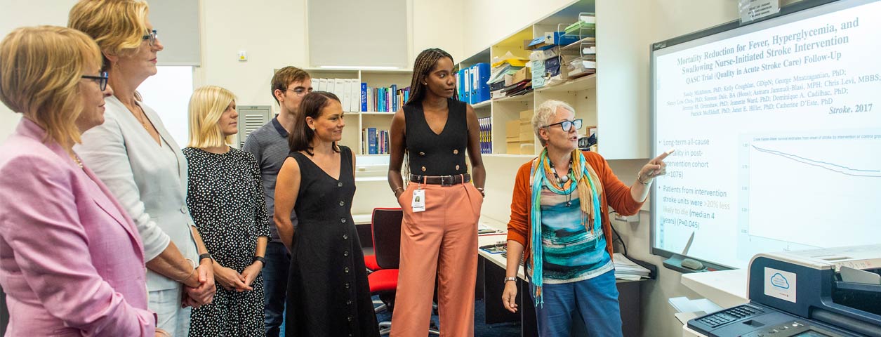 Group of postgraduate students standing around projected slides during a presentation.