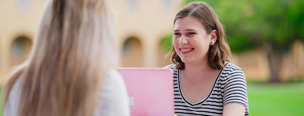 Student on laptop discussing law, business and IT study with friend.