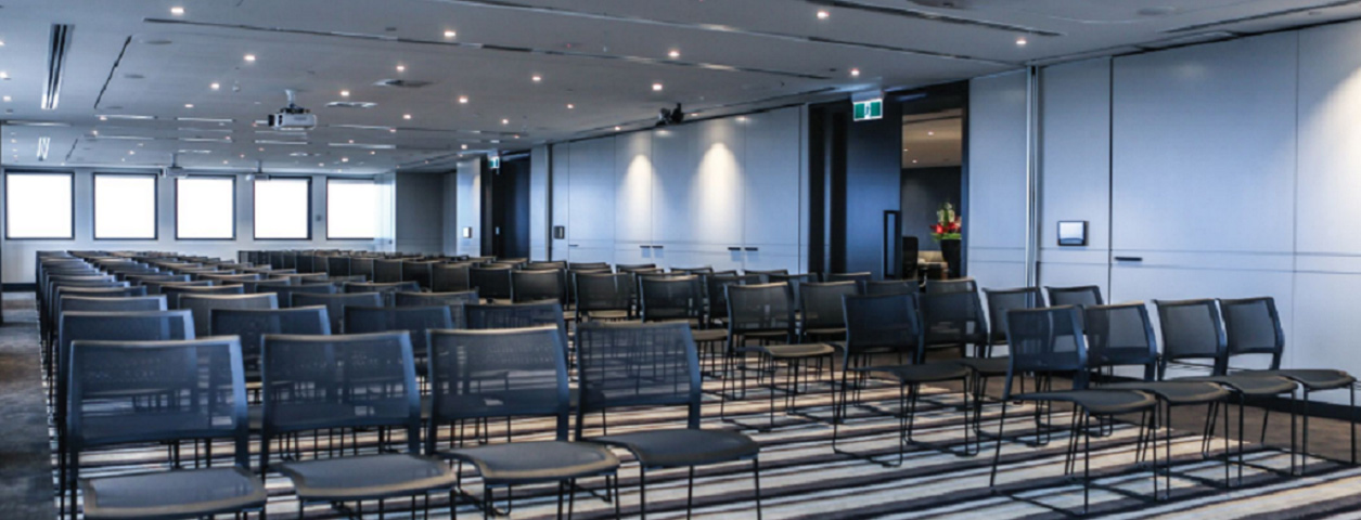 A large room filled with many folding black chairs, set up for some kind of presentation.
