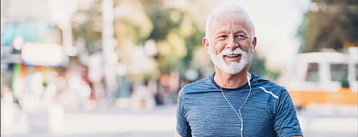 Healthy looking older man walking with headphones. Background is blurred so the focus is on him.
