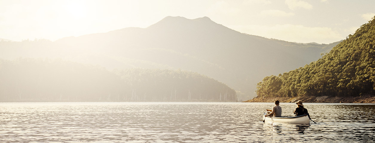 Two people rowing a boat in a lake surrounded by moutains.