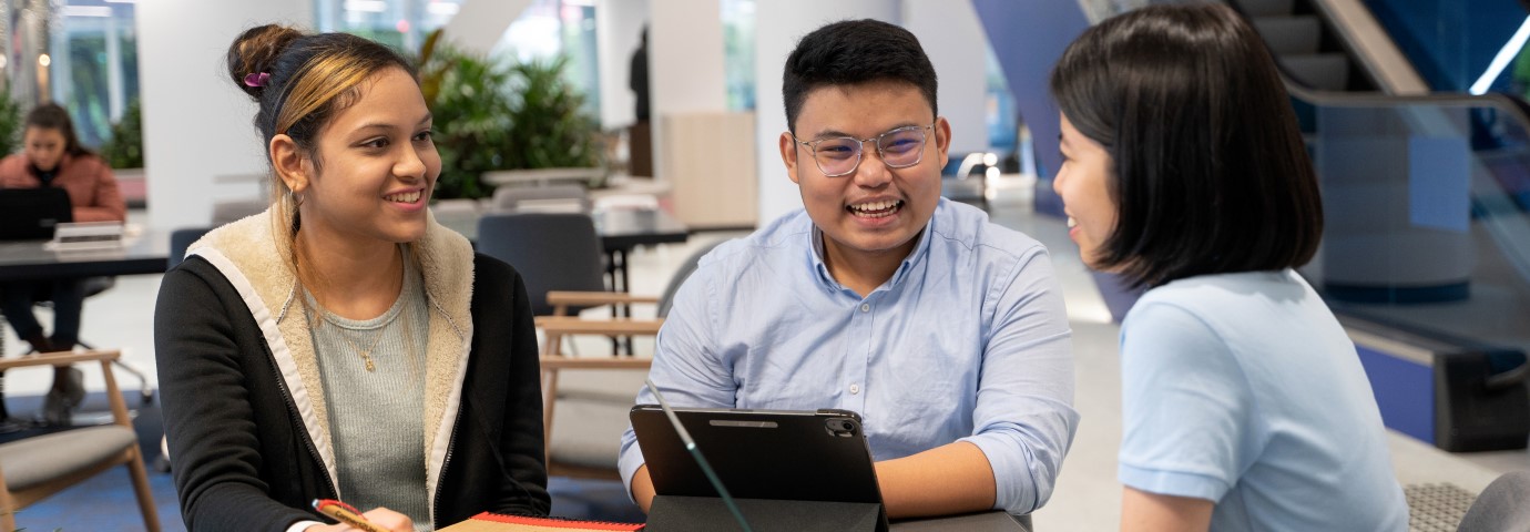 3 international students studying together around a laptop