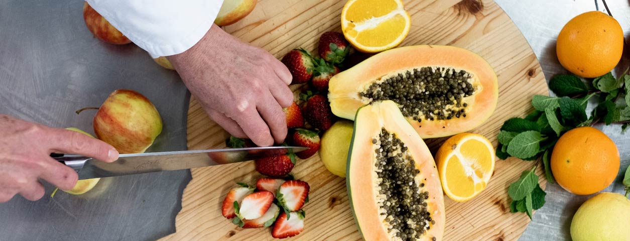 Top-down closeup view of a a chef cutting up fresh fruits on a chopping board.