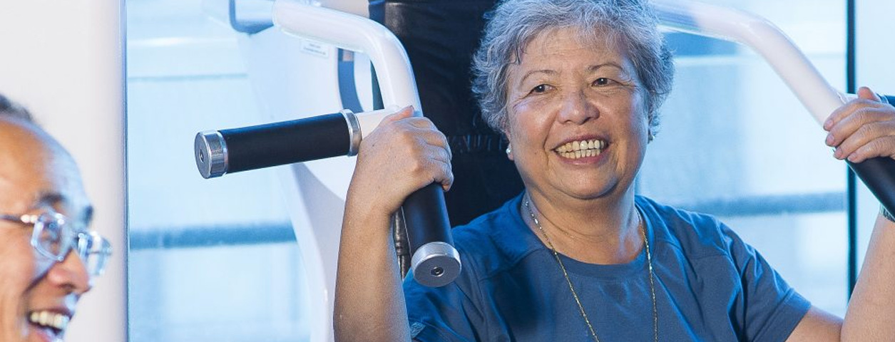 An elderly woman is on an exercise machine, smiling.