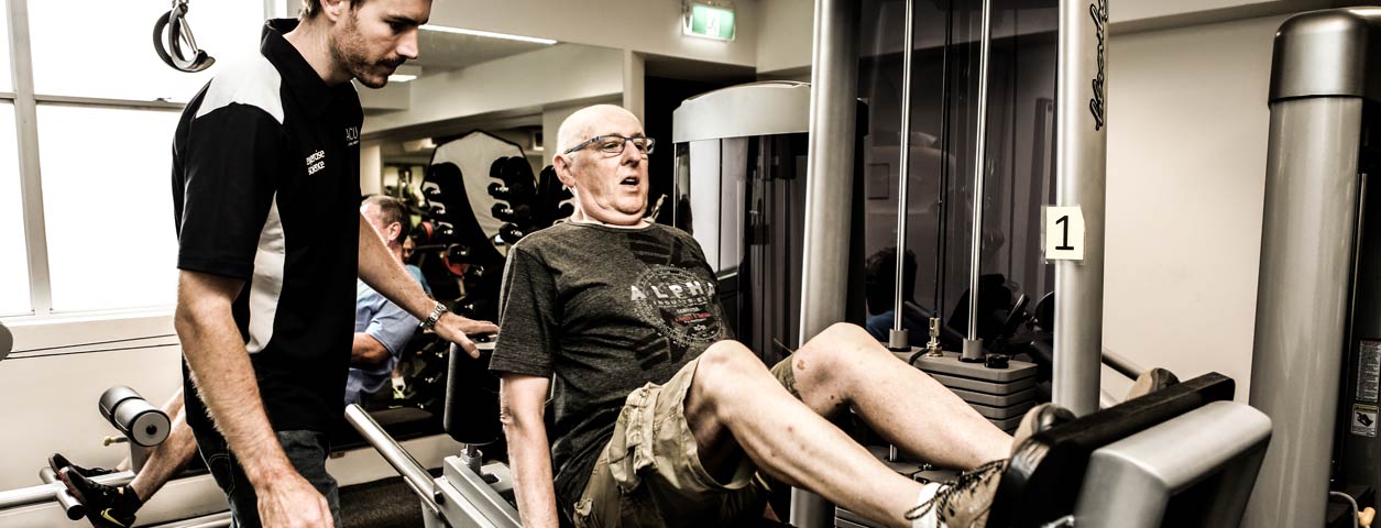 ACU staff personal trainer assisting an adult using gym equipment.