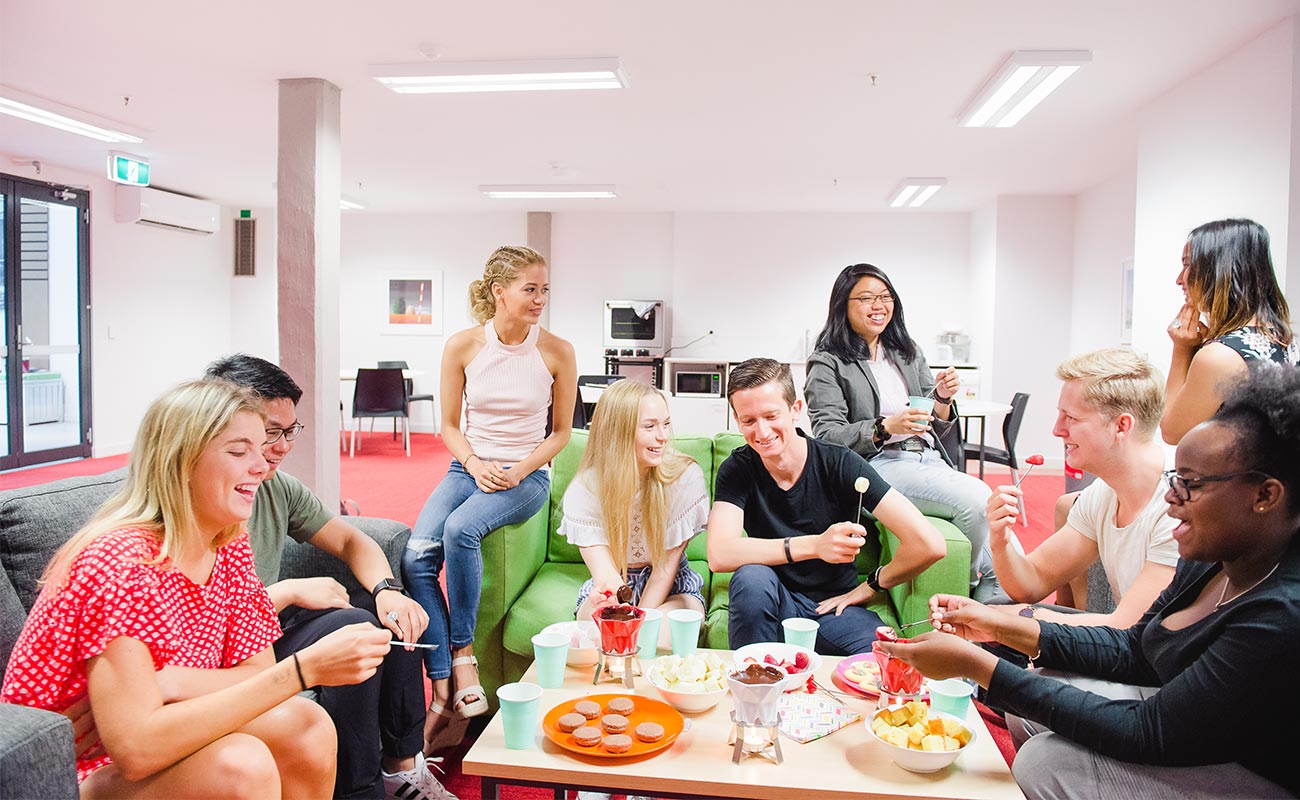 Nine students gather on couches around a table, laughing and chatting as one group.