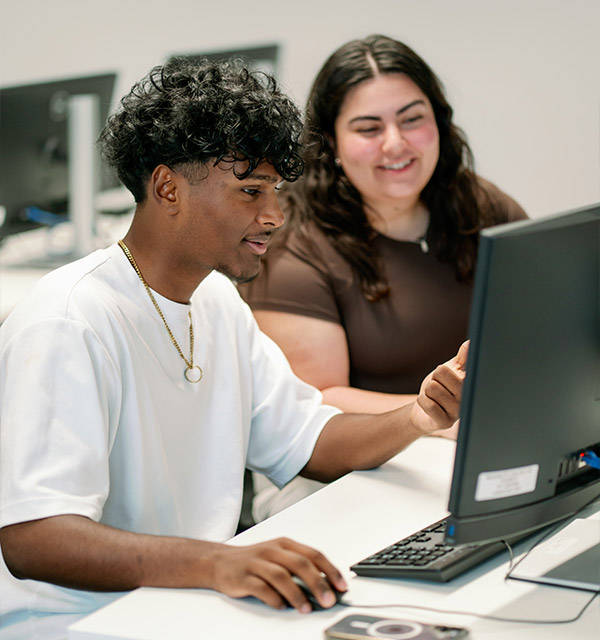 Three people gathered around a computer, smiling and learning