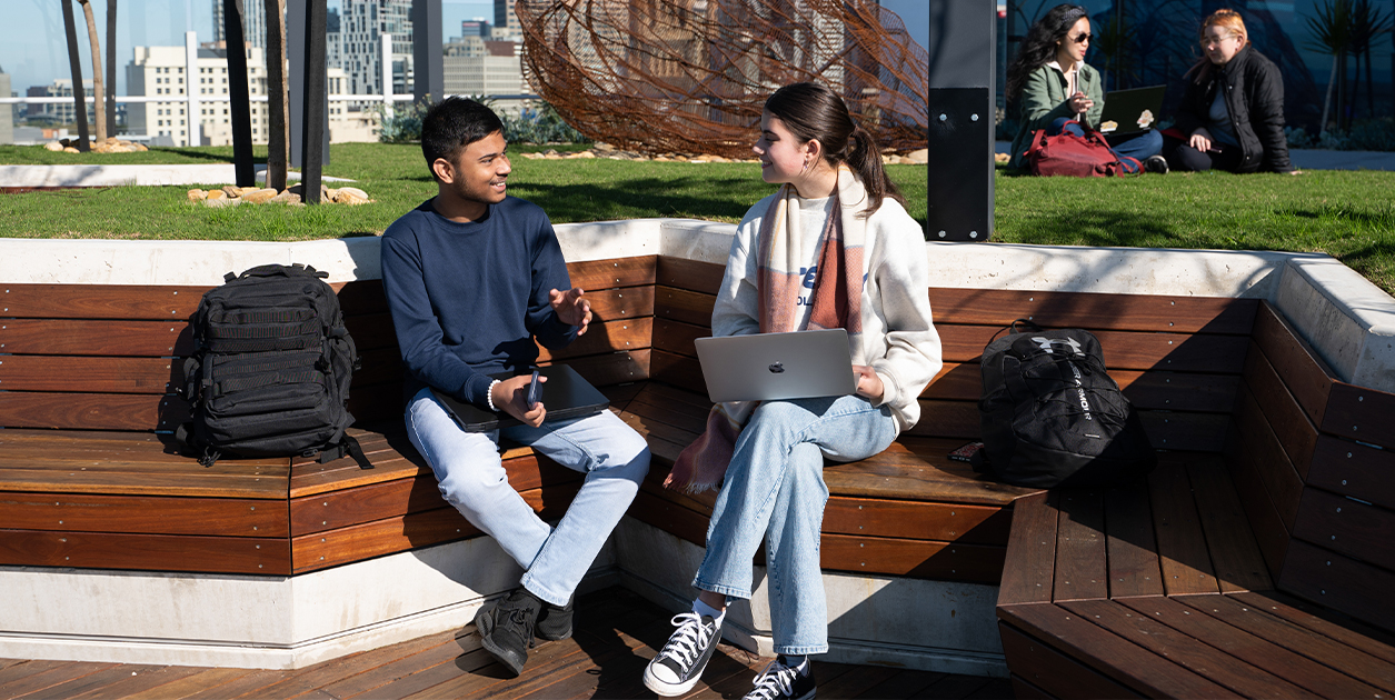 Students on campus sitting outside on a bench.
