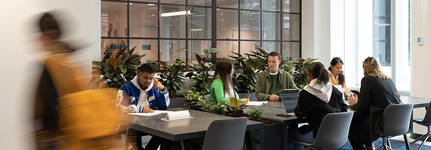 A group students sit at a table talking and working on an ACU campus.