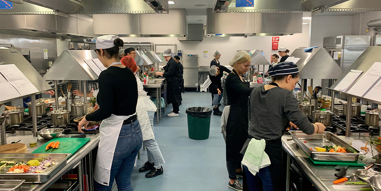 Students in a test kitchen are busy preparing food.