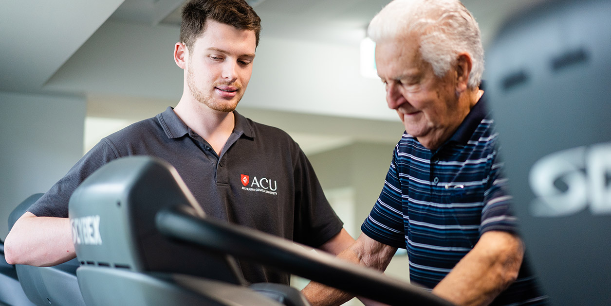 An ACU student assists an elderly patient on a treadmill