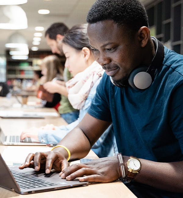 ACU student sitting at a shared desk with a laptop and headphones around his neck