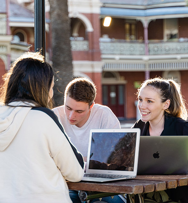 ACU ethics and applied ethics students working at laptops outside on campus