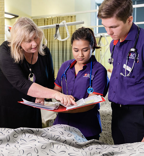 Two ACU students look at a folder while assisted by an instructor in a clinic facility