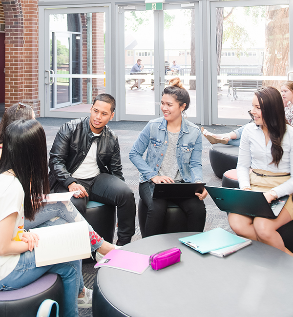 Students sit around a study table with books and laptops