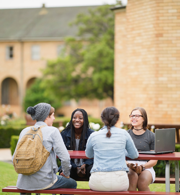 Four students sit around an outdoor table on campus
