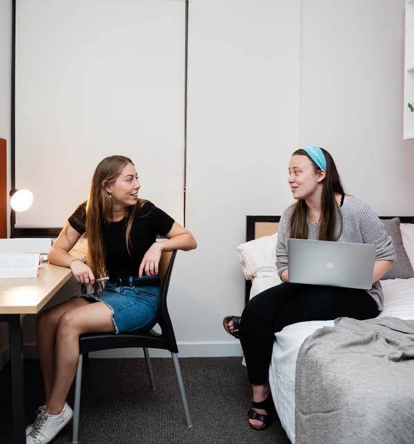 Two students are talking whilst studying in their student accomodation.