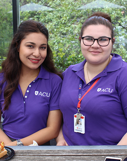 Two ACU students in purple uniform smile.