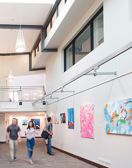 Some people are walking through a hall, its walls hang paintings