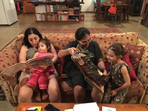 Two women sit on a couch with two girls, reading with them.