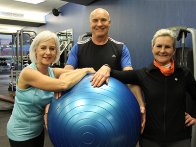 Three older people in exercise gear pose for the camera, each touching a large exercise ball.