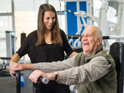 An elderly man is encouraged on an exercise bike by a researcher