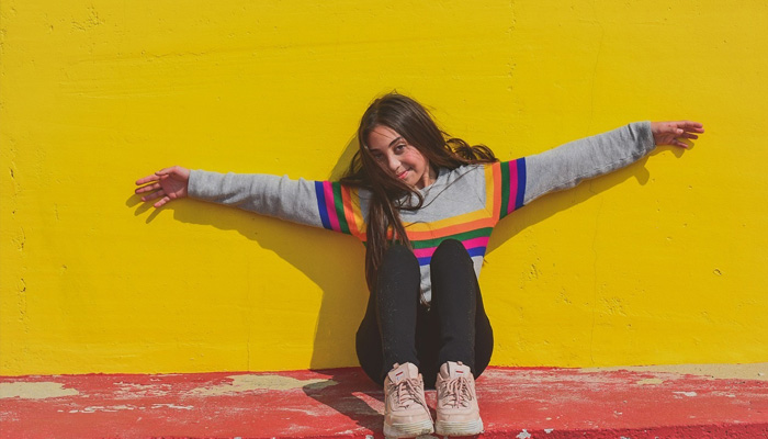 yellow and ochre wall with teen girl siting with her arms out in front of the wall