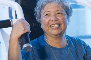 An elderly woman smiles on an exercise machine.