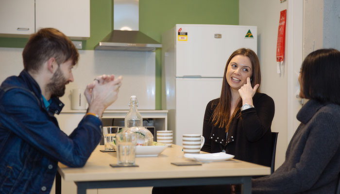 Three student roommates talk around a communal dining table.