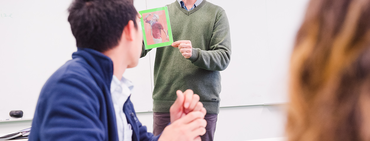 Students in the foreground look on at a teacher in front of a whiteboard