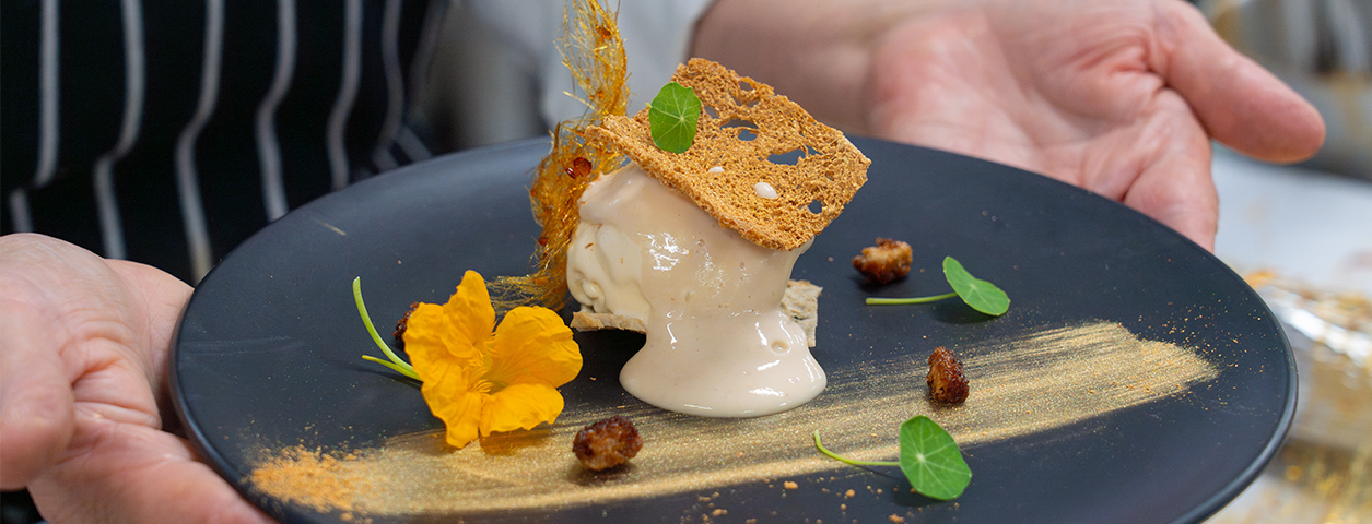 Two hands hold a plate showing off an intricate dessert.